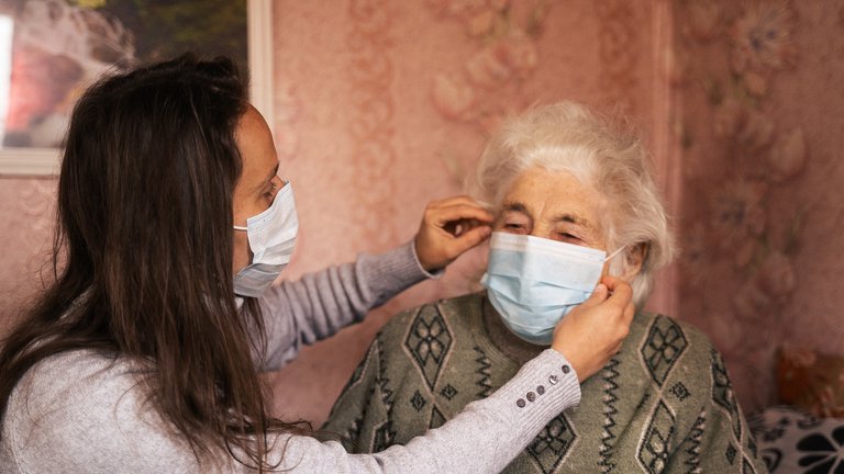Woman adjusts the mask of an older woman.