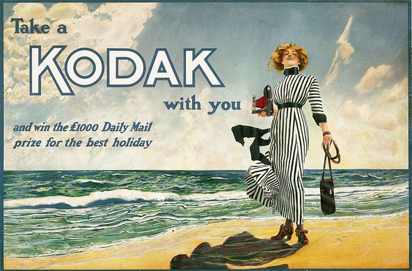Colourful advertisement poster for Kodak showing an illustration of stylish woman in a black-and-white striped dress standing on the beach holding a camera. The text on the poster says: "Take a Kodak with you and win the £1000 Daily Mail prize for best holiday".