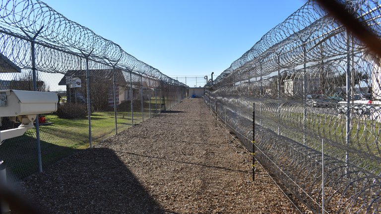 A long stretch of gravel between two barbed-wire fences on a clear sunny day
