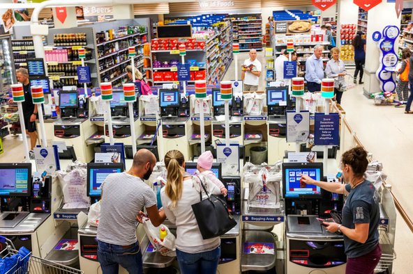 A busy supermarket with a young family using the self-checkout machines in the foreground.